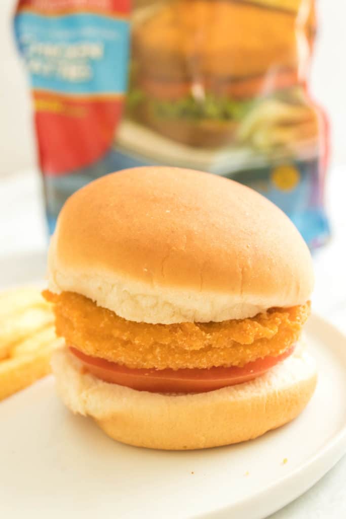 side view: an air fryer tyson chicken patty on a bun with a tomato slice