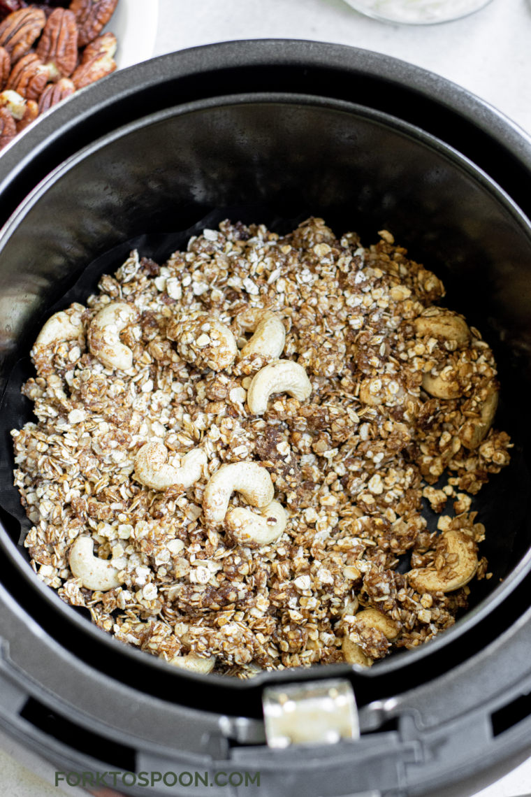 Muesli mixture spread in an even layer on parchment in the air fryer basket