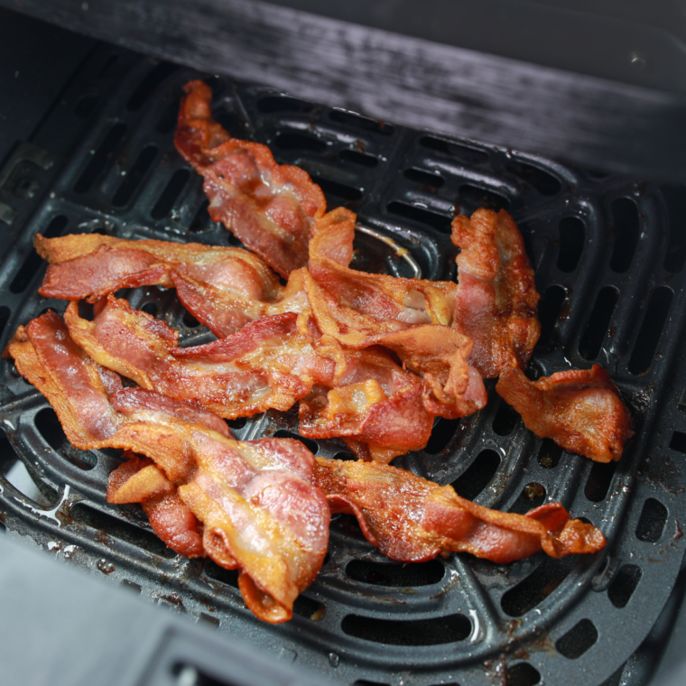 Bacon strips added to the air fryer basket alongside hash browns.