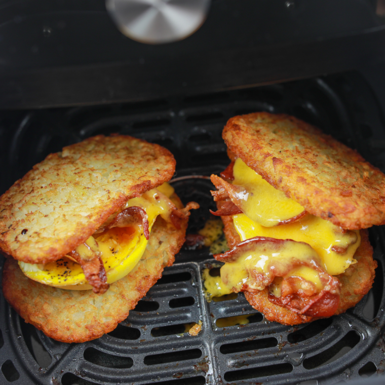 Assembled hash brown breakfast sandwich with bacon, egg, and cheese placed back in the air fryer to melt the cheese.