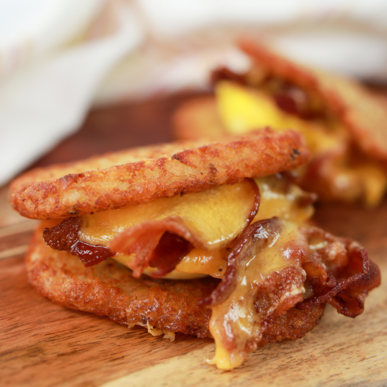 Crispy hash brown breakfast sandwich layered with egg, melted cheese, and sausage, stacked neatly on a plate.