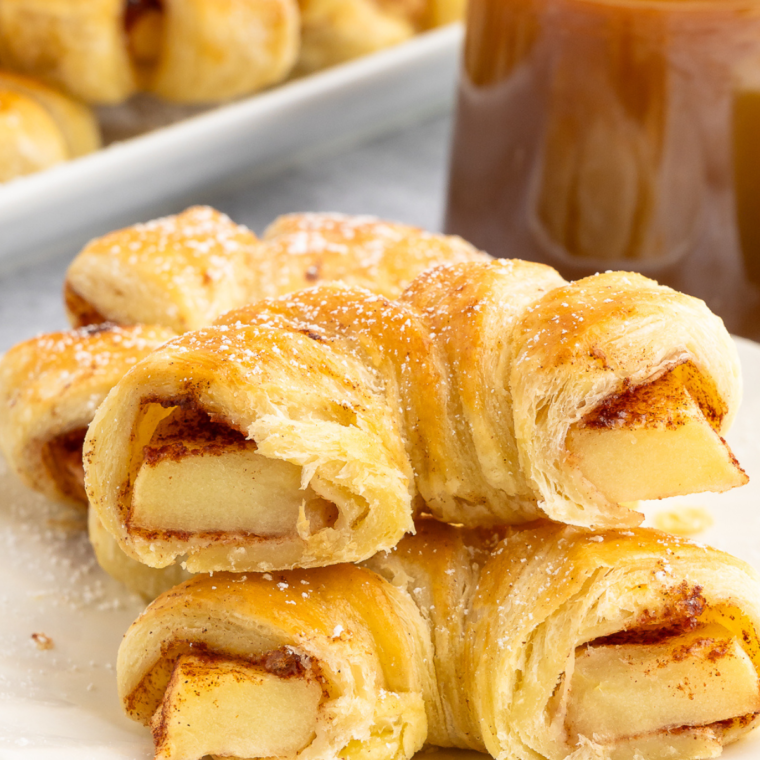 Half of a flaky apple puff pastry ring, revealing soft, cinnamon-spiced apple filling, placed on a white plate.