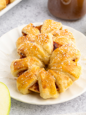 Golden, flaky puff pastry apple rings made in the air fryer, dusted with cinnamon and sugar, served on a white plate.