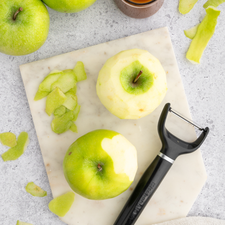 Peeled and cored apples sliced into ¼ inch thick rounds on a cutting board, with a small round cookie cutter nearby.