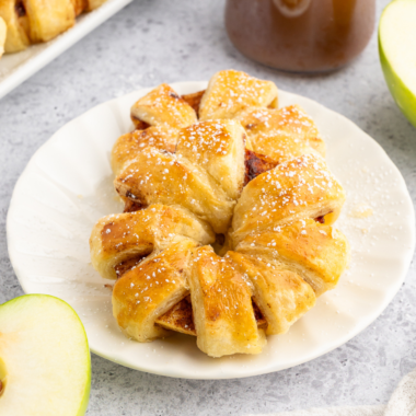 Golden, flaky puff pastry apple rings made in the air fryer, dusted with cinnamon and sugar, served on a white plate.