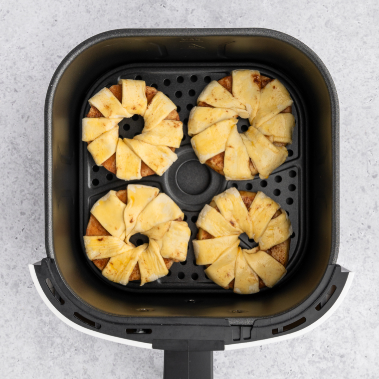 Coated apple slices placed in a single layer in the air fryer basket before cooking.