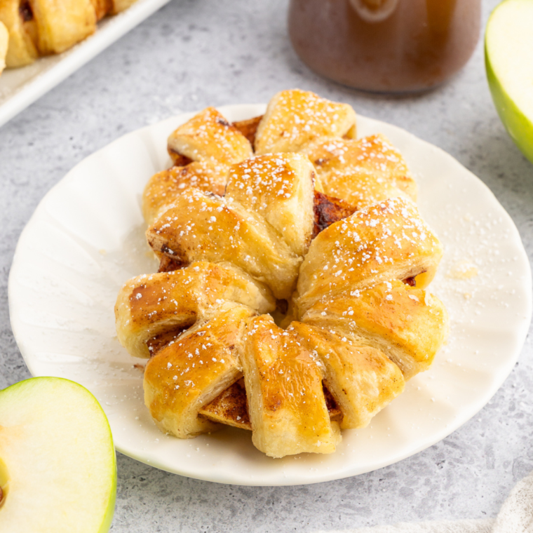 Golden, flaky puff pastry apple rings made in the air fryer, dusted with cinnamon and sugar, served on a white plate.