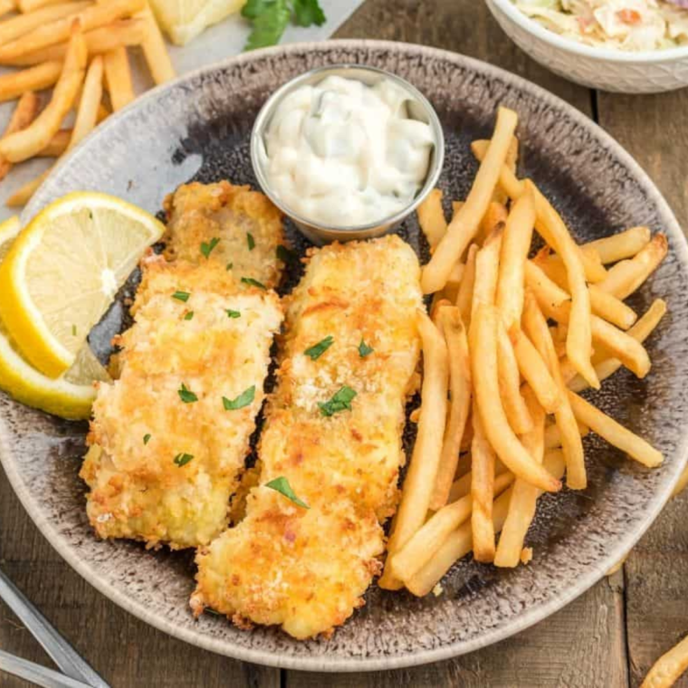 Plate of cooked cod on plate, with a side of tartar sauce, and French fries.