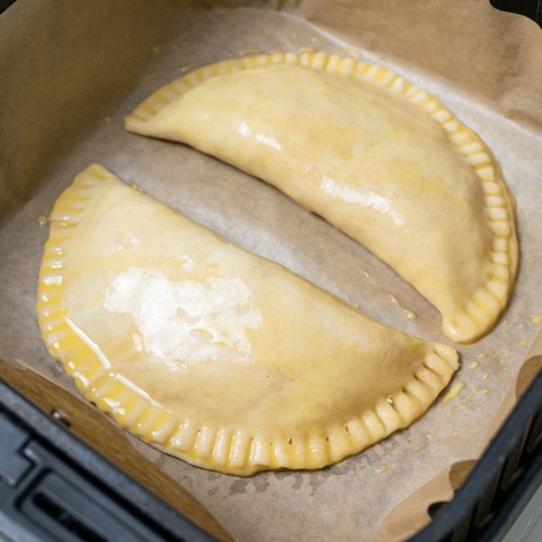 Placing the prepared Cornish Pastries in the air fryer basket for cooking.