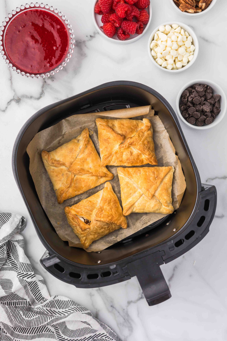 "Golden brown pastry puffs cooking on parchment paper in an air fryer basket."