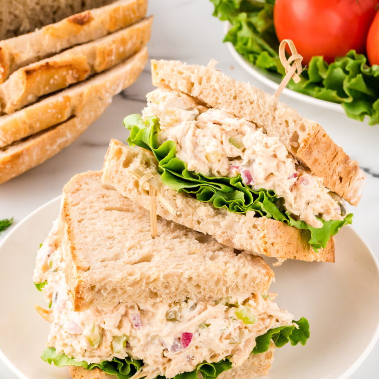A serving of Copycat Chicken Salad Chick Classic Carol on a bed of greens with crackers on the side.