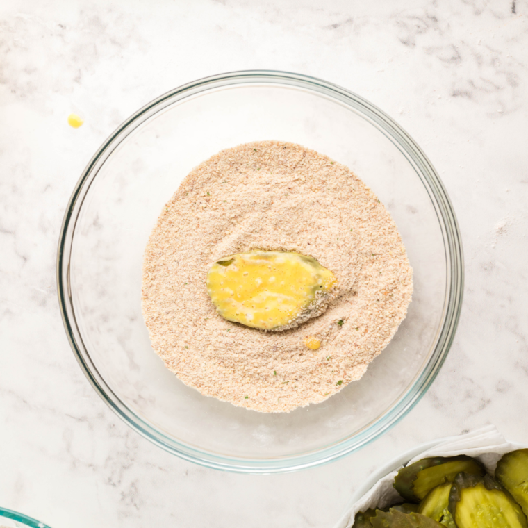 Pickle slice coated with seasoned breadcrumb mixture in a shallow bowl.