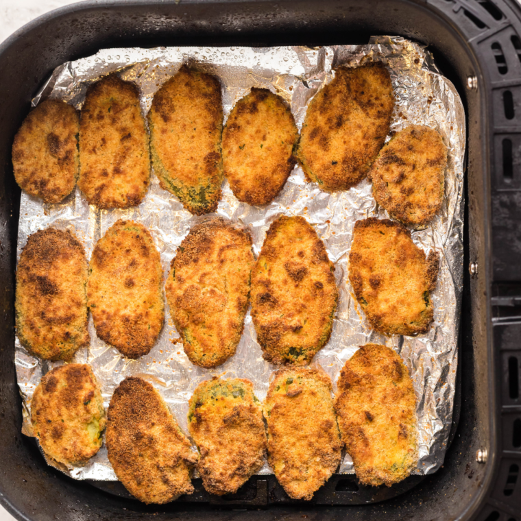 Golden, crispy breaded pickle slices in an air fryer basket, ready to serve as a homemade version of Red Robin's Pickle Nickels.