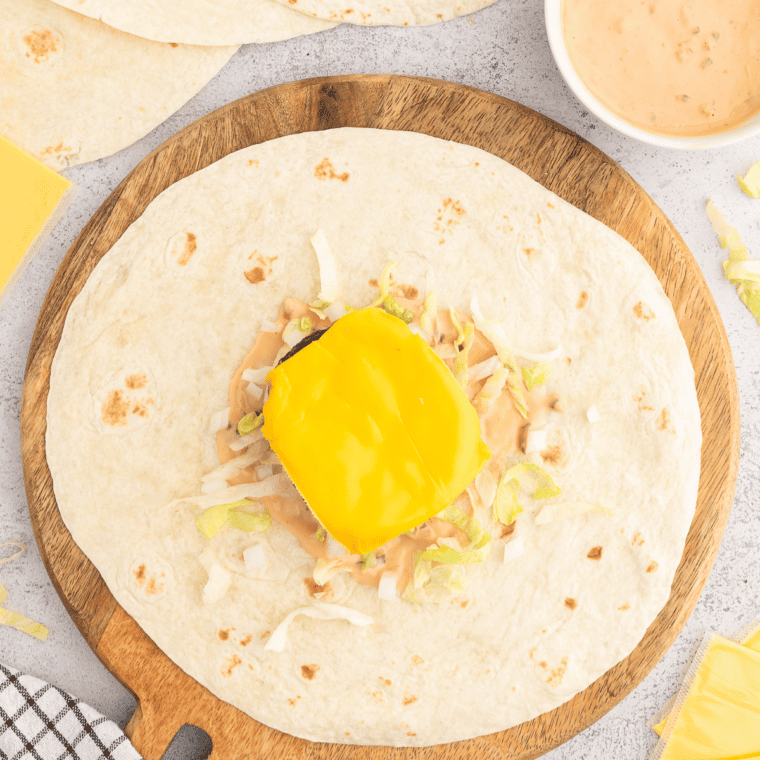 Preparing tortillas with In-N-Out style sauce, layering lettuce, tomato, pickles, onions, and adding a cheese-topped burger patty before folding into a tight wrap.