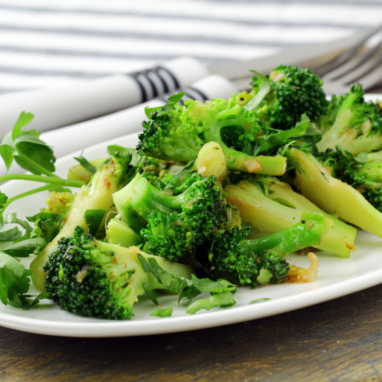 Copycat Longhorn Steakhouse broccoli on a white plate, tender florets coated in garlic butter.