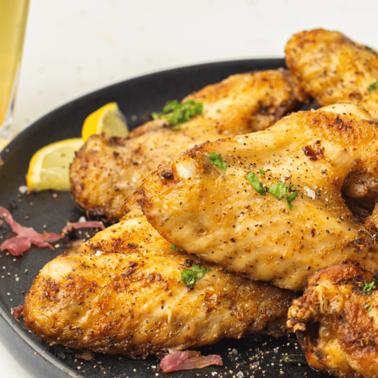 Plate of crispy Wingstop Lemon Pepper Wings garnished with lemon slices and sprinkled with fresh herbs.