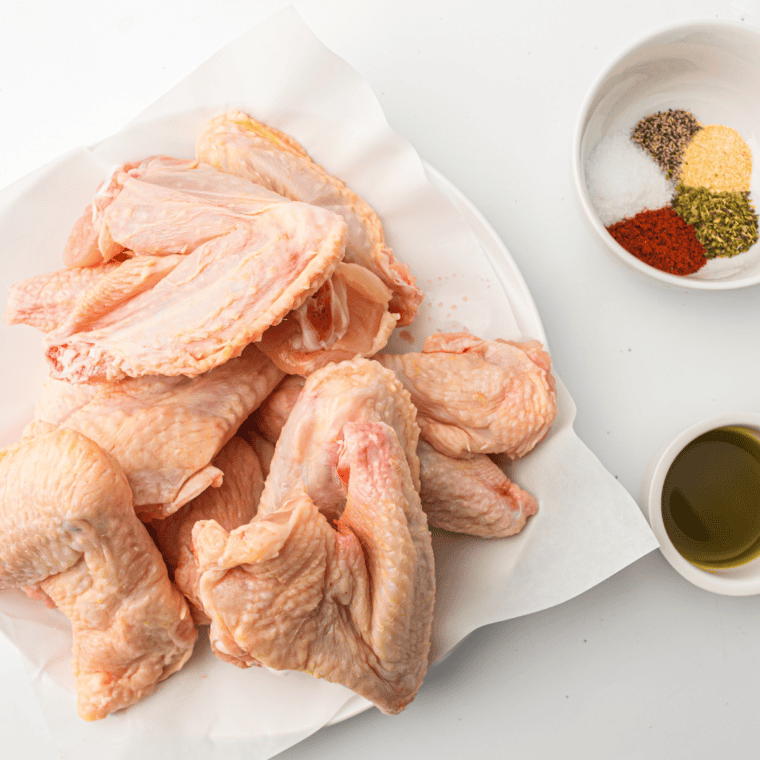 Chicken wings, lemon pepper seasoning, butter, garlic powder, olive oil and salt arranged on a wooden board.