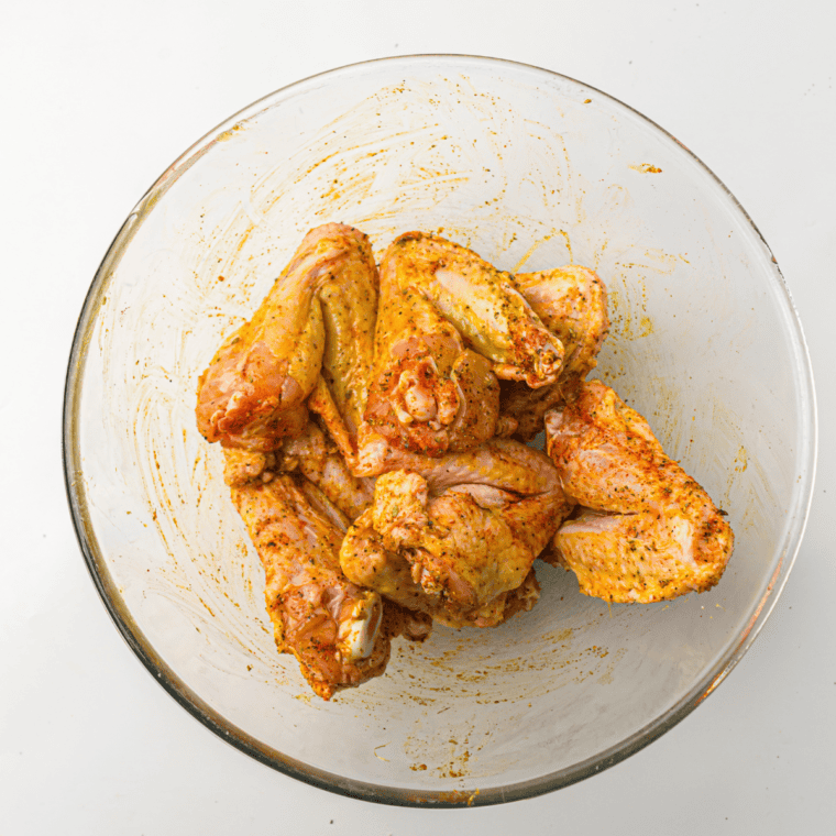 Seasoned chicken wings on a cutting board next to an air fryer preheating to 400°F.