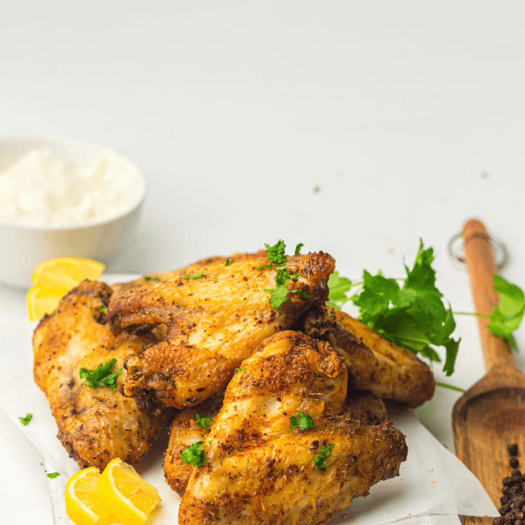Plate of crispy Wingstop Lemon Pepper Wings with lemon slices and sprinkled with fresh herbs.
