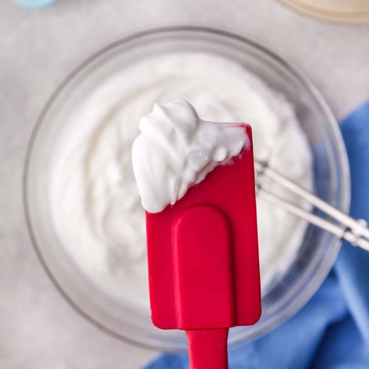 Beating egg whites with an electric mixer until glossy, stiff peaks form for light and fluffy cloud bread chips.