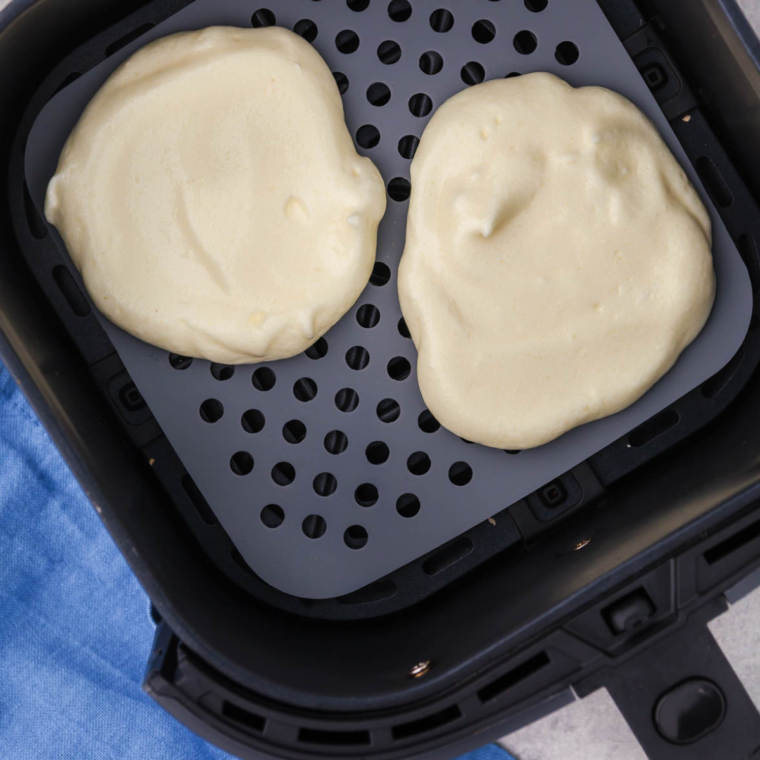 Placing parchment paper or silicone mats in the air fryer basket before spooning cloud bread mixture into rounds and air frying at 300°F for 10-12 minutes until golden and crispy.