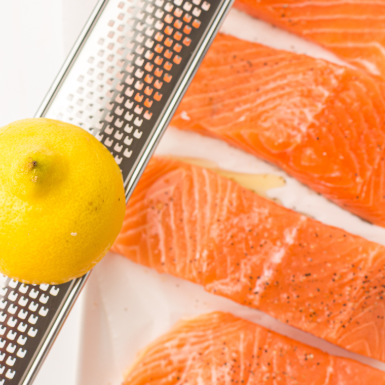Raw salmon fillets being seasoned with olive oil, garlic powder, salt, pepper and lemon