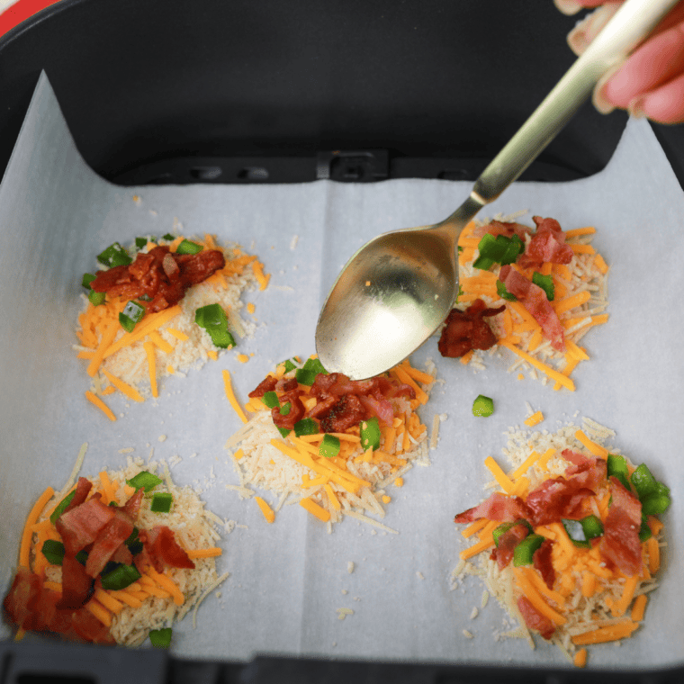 Parmesan and cheddar piled onto parchment paper, topped with diced jalapeño and bacon before air frying.