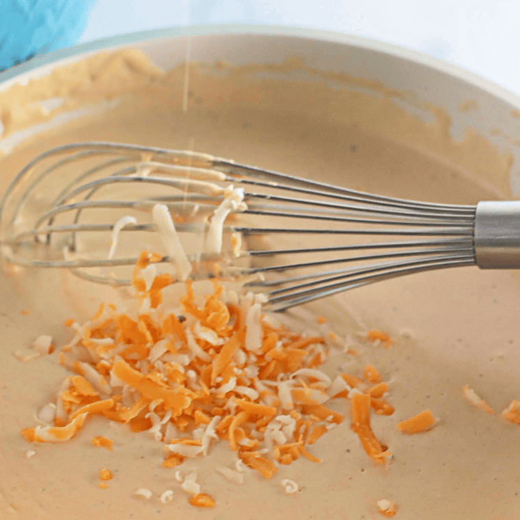 Adding shredded cheddar, Monterey Jack, and Velveeta cubes to a creamy cheese sauce, then stirring in cooked macaroni until fully coated.