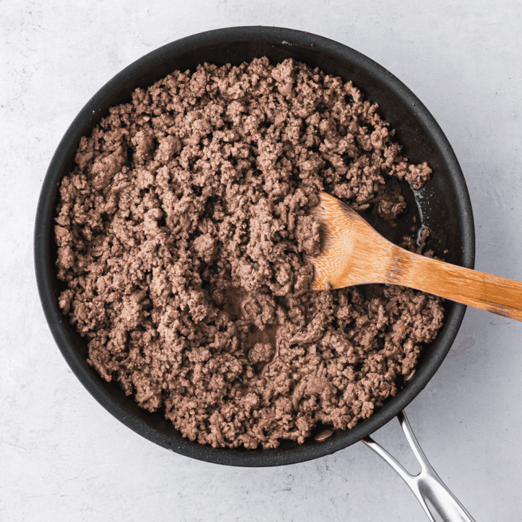 Ground beef cooking in a pan with onions, garlic, and taco seasoning, stirred together until browned and flavorful.