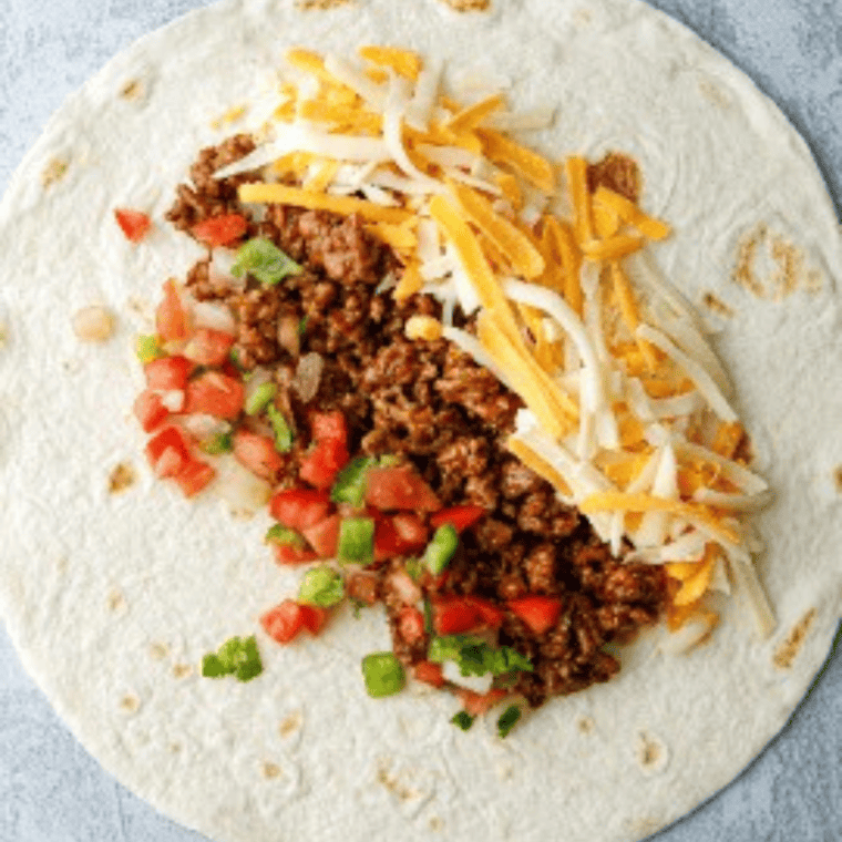 Flour tortilla laid flat with seasoned beef and shredded cheese in the center, ready to be rolled into a chimichanga.