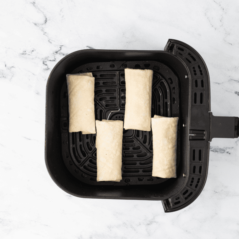 Chimichangas placed seam side down in an air fryer basket, set to cook at 375°F until golden brown and crispy.