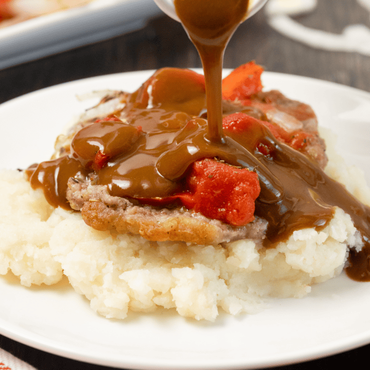 Juicy Swiss steak cooked in the air fryer, covered in a savory tomato gravy and served with mashed potatoes.