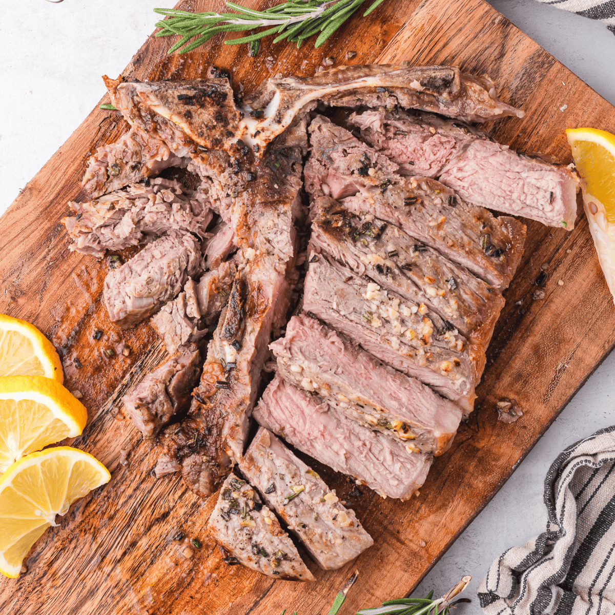 A perfectly grilled Bistecca Alla Fiorentina (Florentine steak) with a golden crust, served on a wooden board with fresh rosemary and lemon wedges.