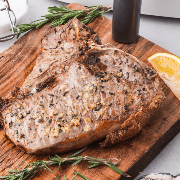 A perfectly cooked Bistecca Alla Fiorentina, seared golden brown with a juicy center, served on a wooden board with fresh rosemary and lemon wedges.