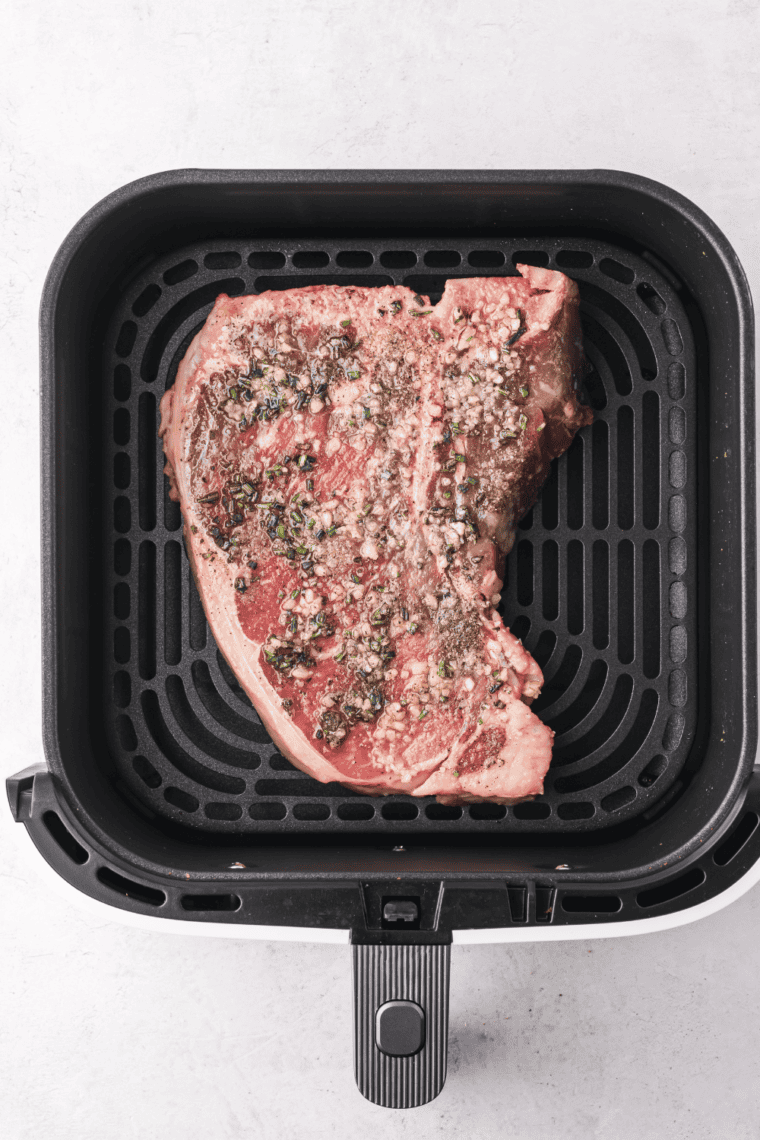 Seasoned T-bone steak placed in an air fryer basket, cooking to desired doneness with a meat thermometer for accuracy.