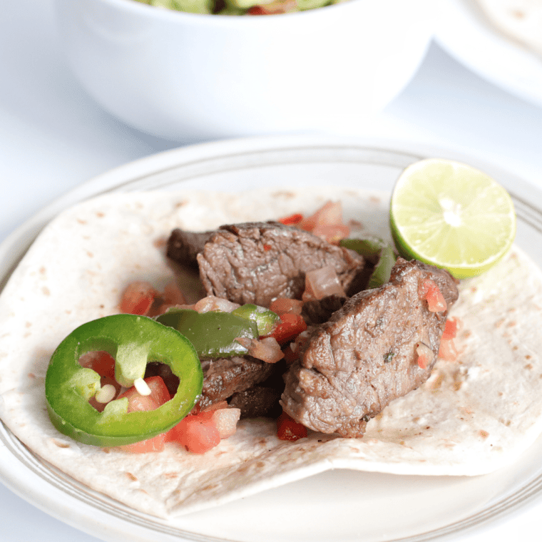 A skillet of Copycat Chili's steak fajitas with seared steak, colorful bell peppers, and sweet onions.