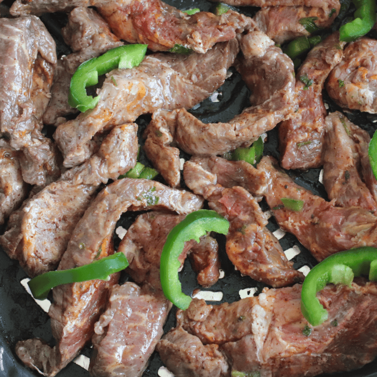 Marinated flank steak cooking in an air fryer basket at 400°F for Copycat Chili's steak fajitas.