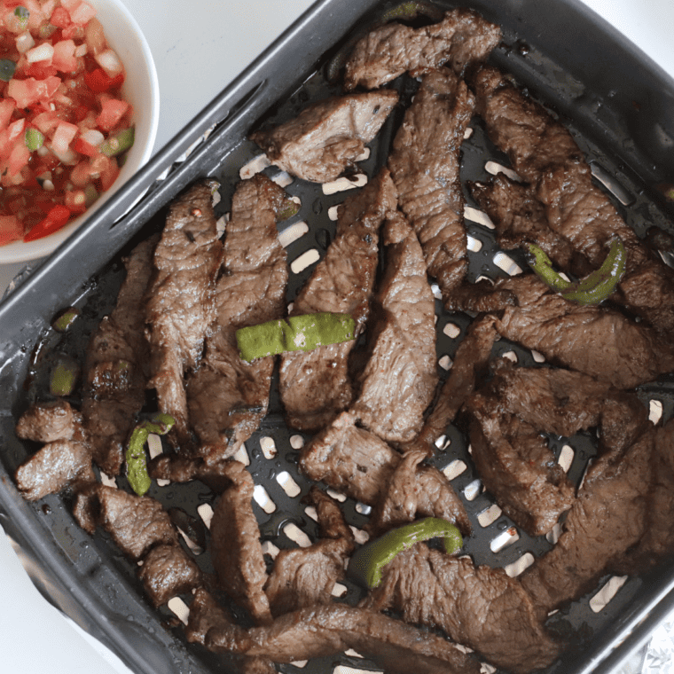 Sliced bell peppers and onions air frying at 380°F until tender and charred for steak fajitas.