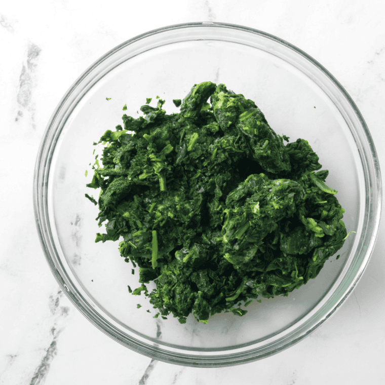 Frozen spinach drained after being squeezed out, in a large glass mixing bowl.