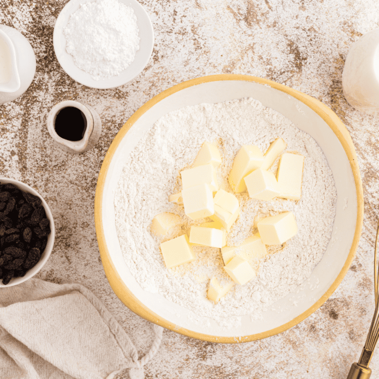 Mixing self-rising flour, sugar, cinnamon, and grated butter to create a biscuit dough with buttermilk and raisins.