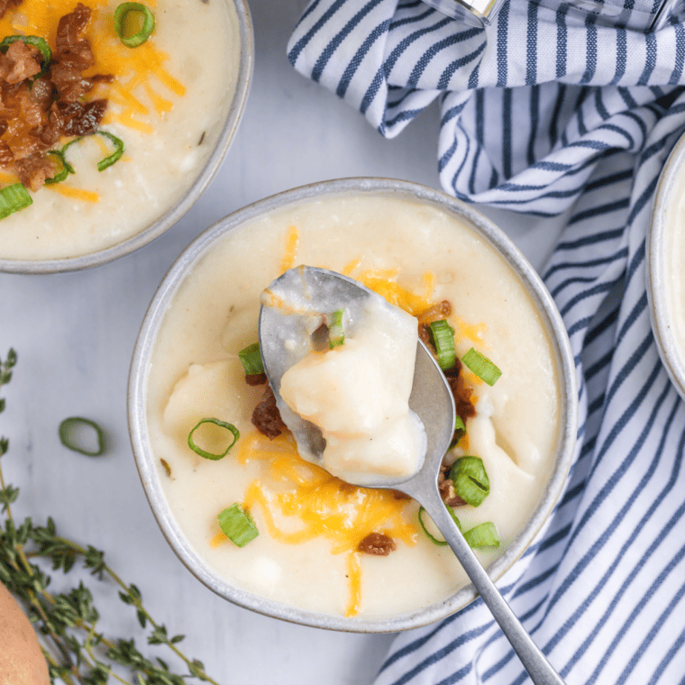 Instant Pot Panera Baked Potato Soup garnished with crispy bacon, green onions, and shredded cheese in a bowl.