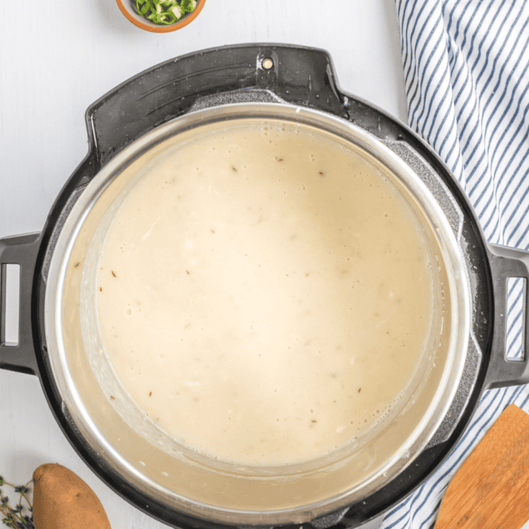 Using a potato masher to mash potatoes and blend in cream and cheese.
