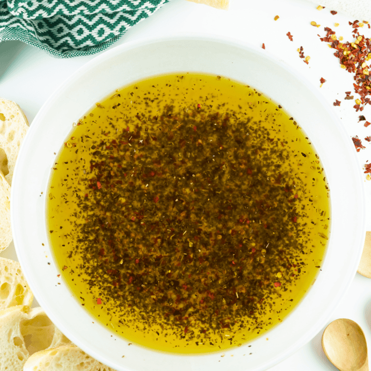 A close-up of a bowl of Johnny Carino's Olive Oil Dip with fresh herbs and spices, perfect for dipping bread.