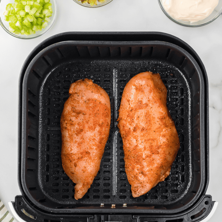 Seasoned chicken breasts in an air fryer basket, cooking at 375°F until golden and juicy, ready to be chopped for salad.