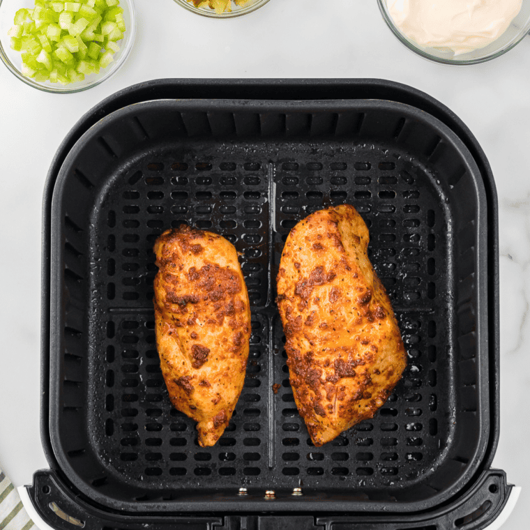 Air fryer cooking seasoned chicken breasts at 375°F until golden, juicy, and ready for chopping.