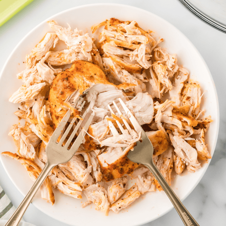 Shredding cooked chicken in a white mixing bowl.