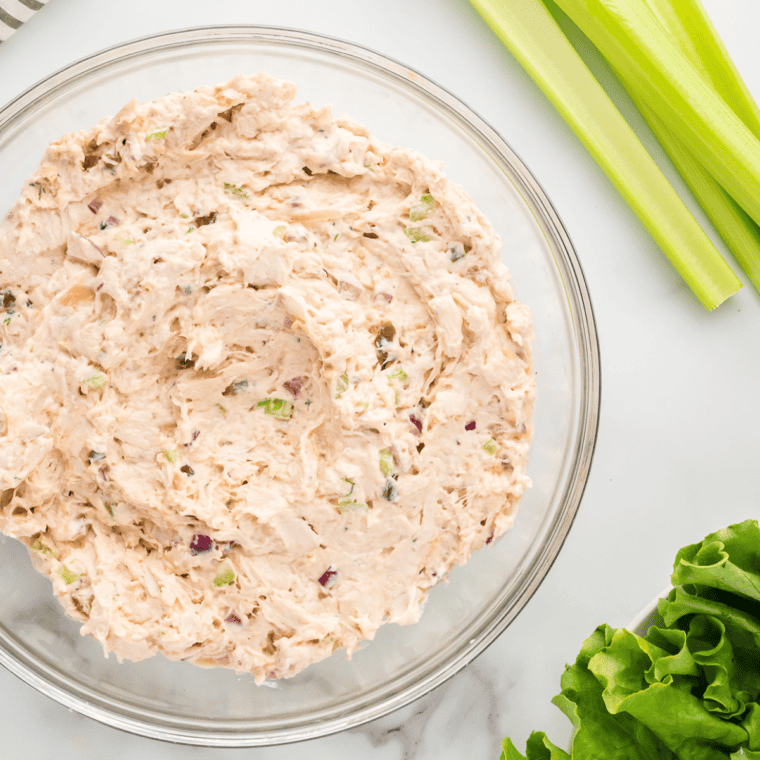 Chopped chicken, toasted almonds, celery, and grapes mixed with creamy dressing in a large bowl.