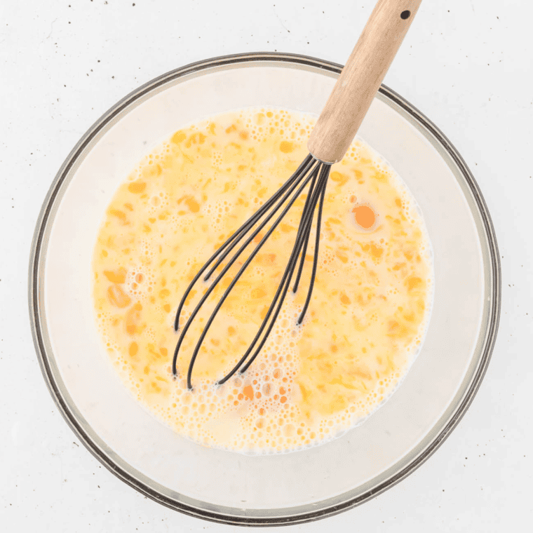 Whisking eggs and milk in a glass bowl for a breakfast casserole