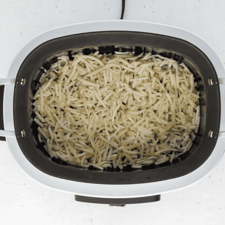 Shredded hash browns spread across the bottom of a slow cooker