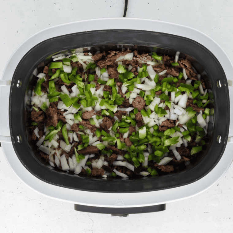 Cooked sausage, peppers, and onions layered over hash browns in a crockpot